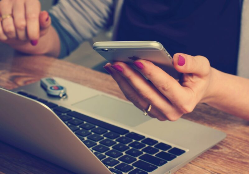 a woman using her phone while working on the laptop