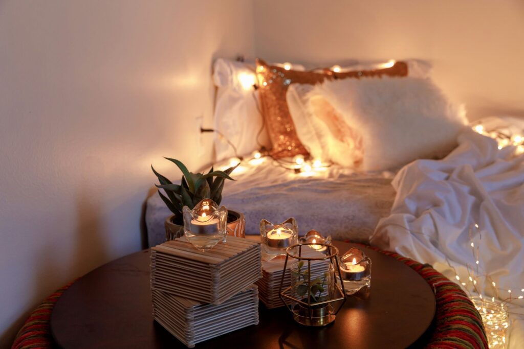 a cozy setup of a bed with pillows and a comforter. Plants and candles on the side table