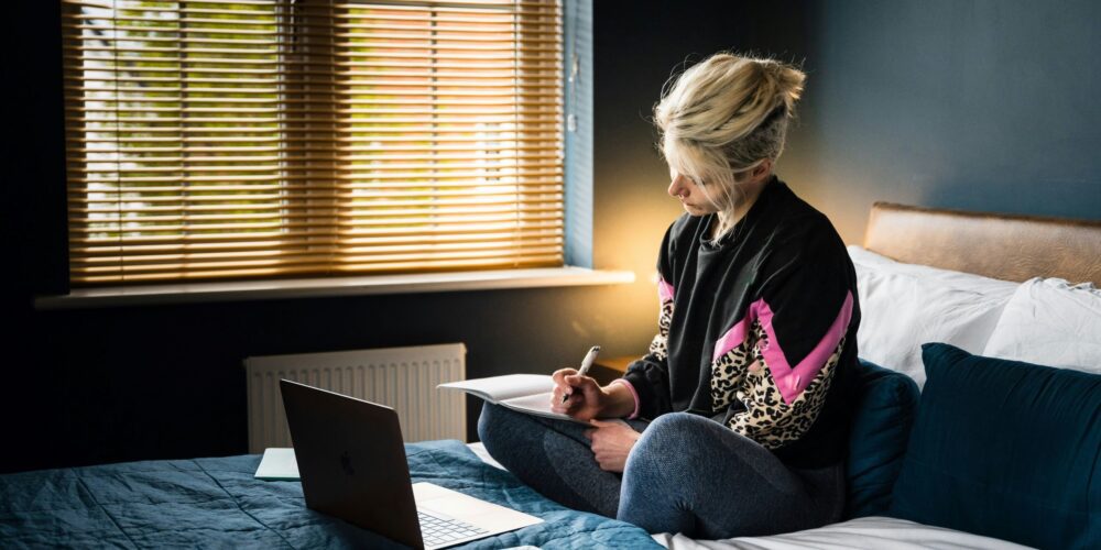 a girl writing her productivity journal while working on her laptop