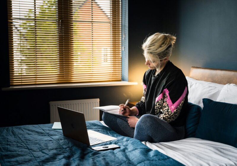 a girl writing her productivity journal while working on her laptop