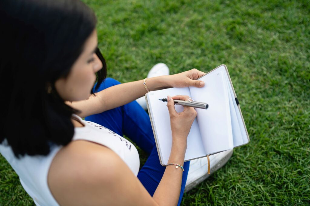 a girl sitting in a park practicing self-care through journaling