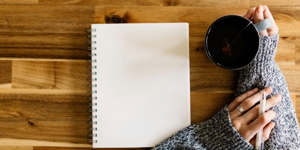 a woman holding a pen next to a journal wondering if journaling can be a hobby