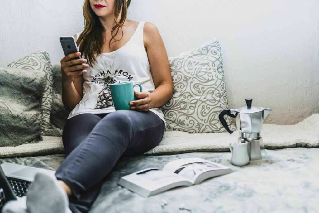 A young woman sipping coffee and scrolling her phone in bed, a reminder of how we often start the day and why mindful morning habits matter.