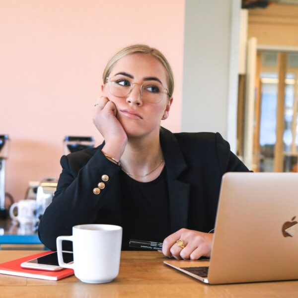A thoughtful woman sits at her work desk with a coffee mug and laptop, representing the mental load and daily reflections of a 9-5 job routine.