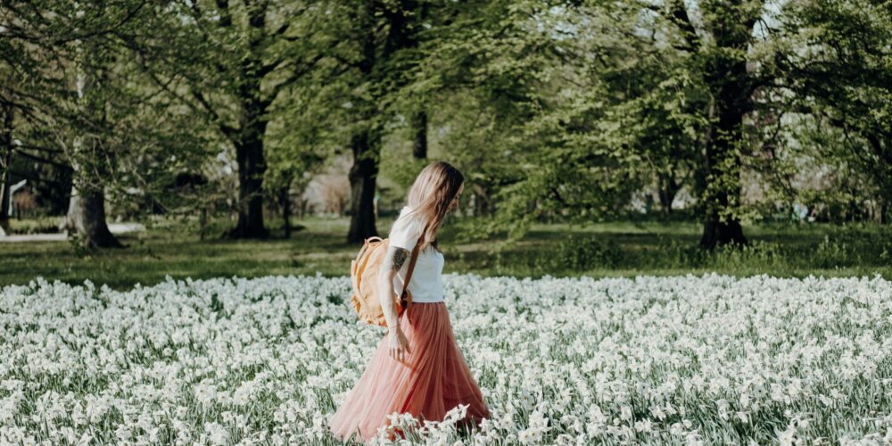 A woman gently walking through a field of flowers during early morning hours, wearing light and airy clothing that reflects the warmth of spring.