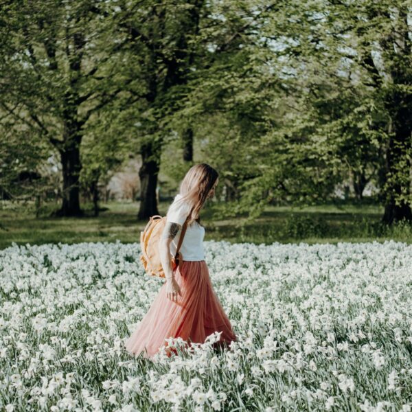 A woman gently walking through a field of flowers during early morning hours, wearing light and airy clothing that reflects the warmth of spring.
