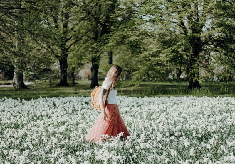 A woman gently walking through a field of flowers during early morning hours, wearing light and airy clothing that reflects the warmth of spring.