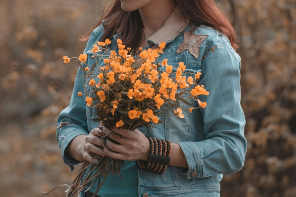 A young woman standing in a blooming spring garden surrounded by colorful flowers, sunlight softly falling on her face.