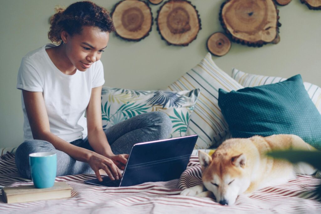 A woman sitting by a large window with her laptop, surrounded by natural spring elements like fresh flowers and greenery