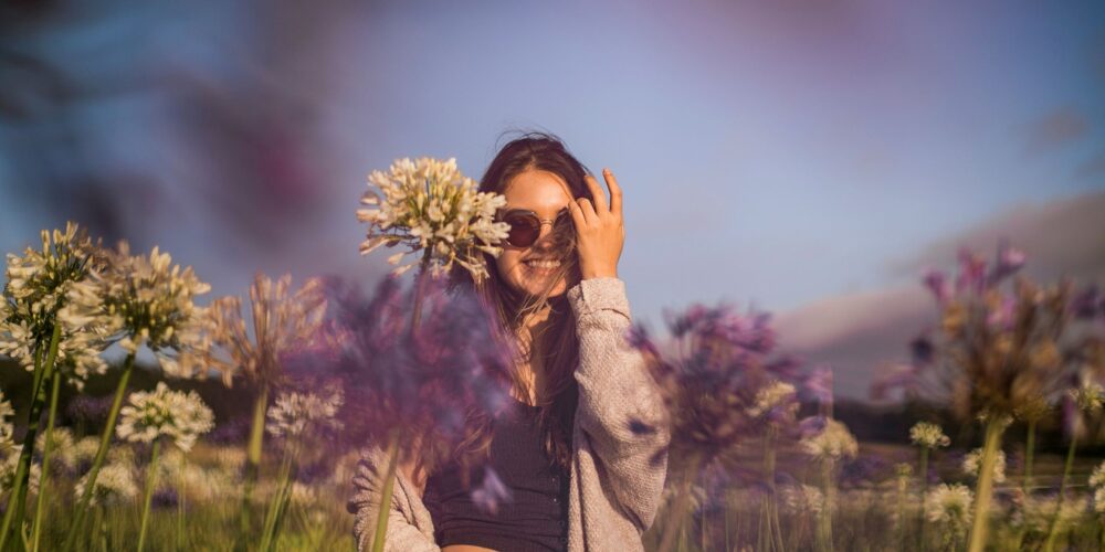 A young woman standing in a blooming spring garden filled with soft pastel flowers, gently touching petals with her fingertips.