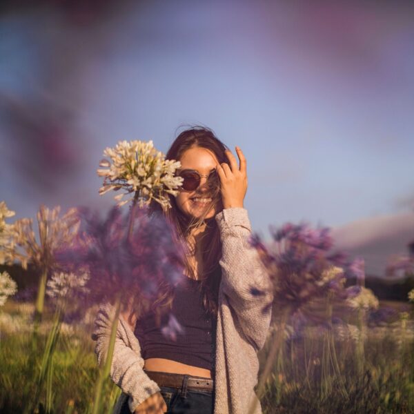 A young woman standing in a blooming spring garden filled with soft pastel flowers, gently touching petals with her fingertips.